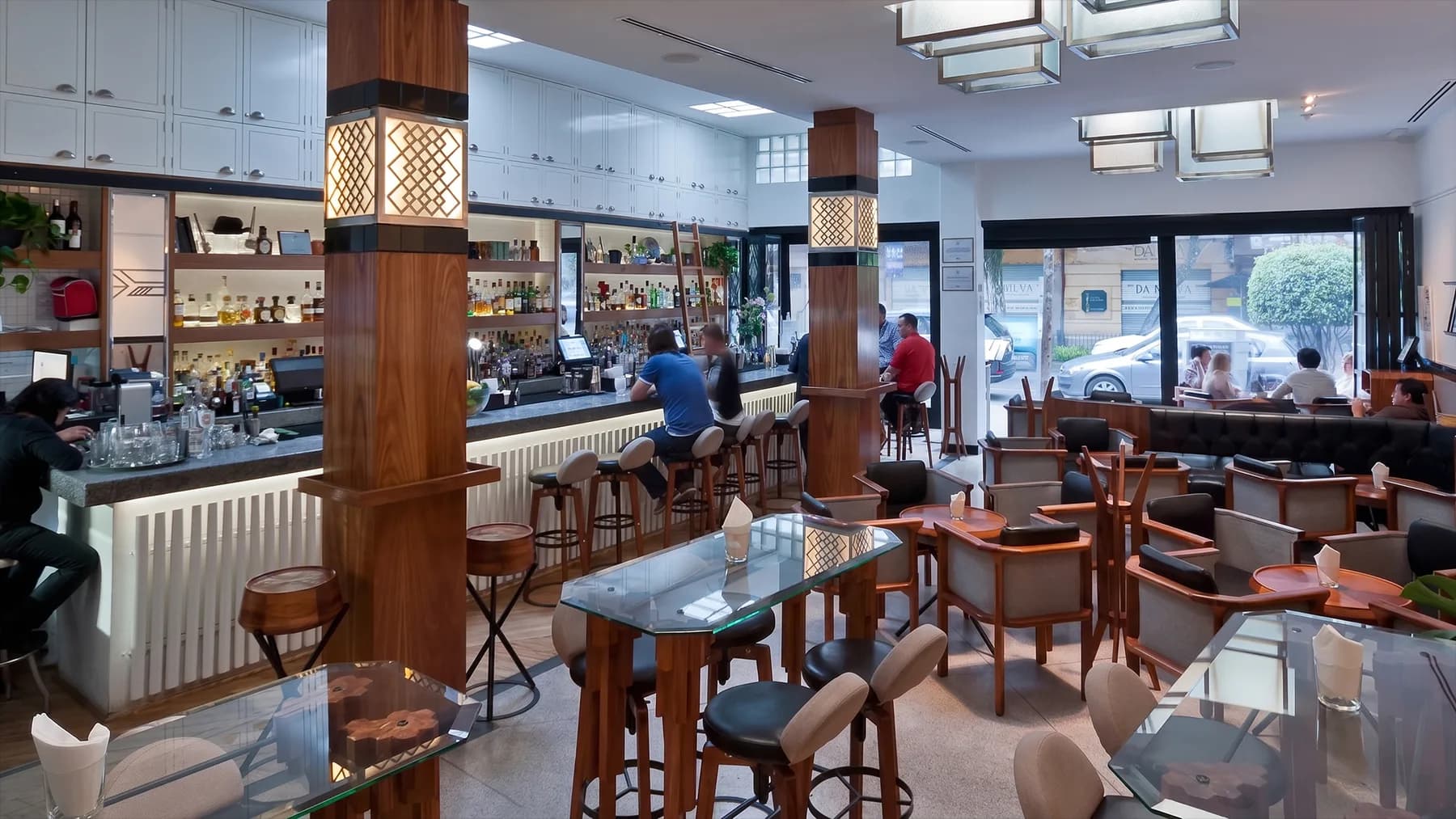 El salón principal de Limantour Polanco: invitados en la barra, columnas de nogal con faroles Art Deco encendidos y mesas con cubierta de cristal