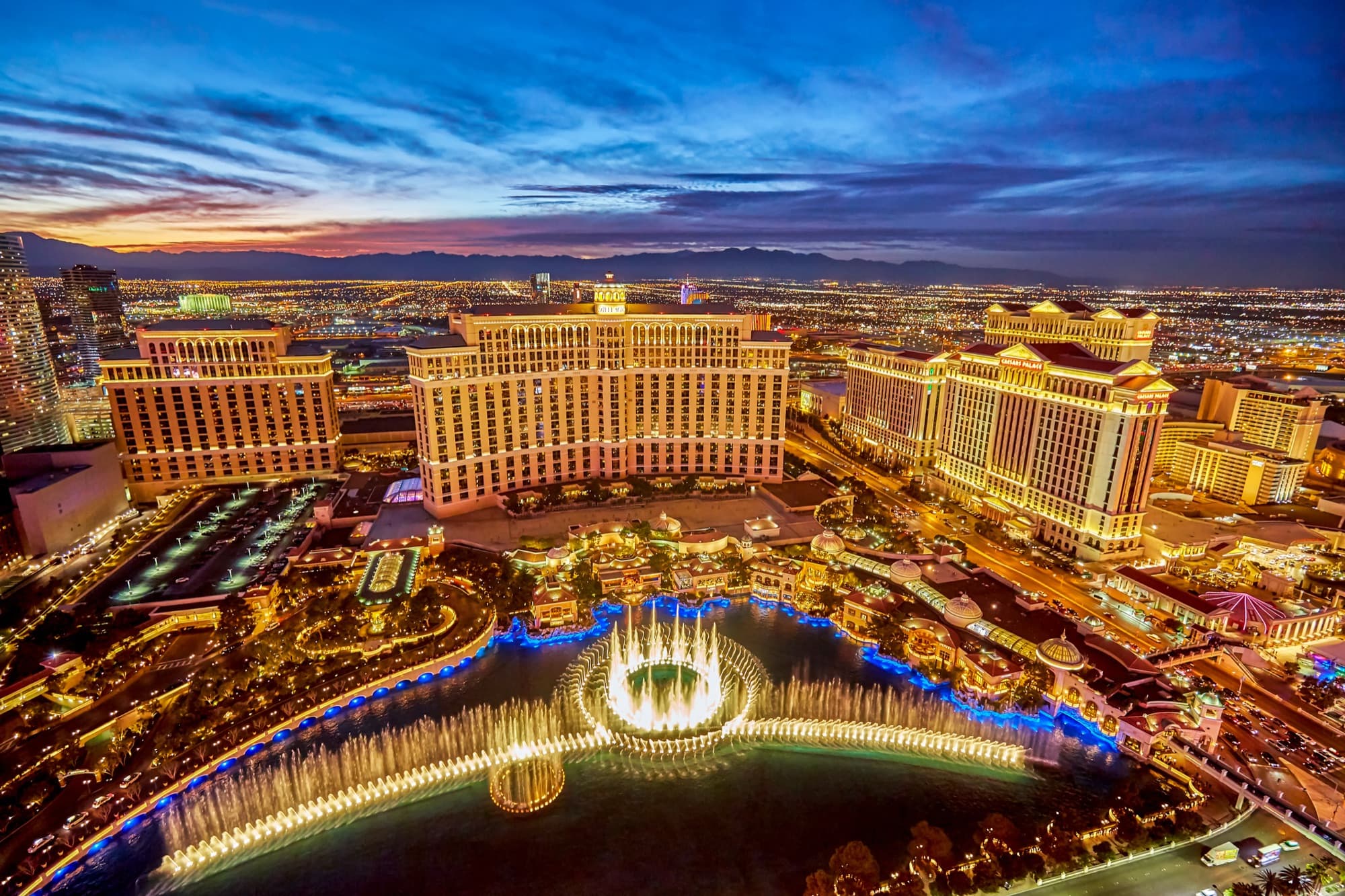 Aerial view of the Bellagio Resort & Casino and the Las Vegas Strip at dusk with the iconic fountains illuminated in the foreground