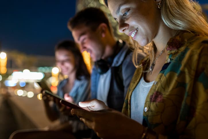 Group of friends engaged in conversation on their phones at night, illuminated by city lights