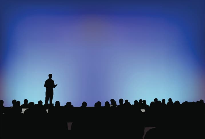 Silhouette of a keynote speaker on stage addressing a conference audience