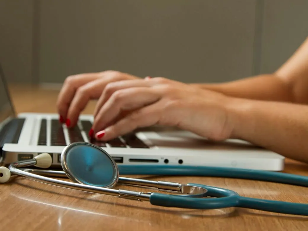 A clinician at a laptop, a stethoscope beside it
